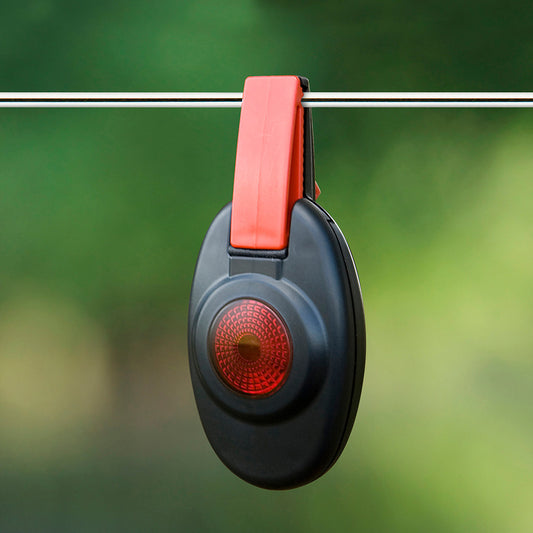 Patriot fence alert waring light is a Black and red clip-on device hanging on a wire with a green blurred background