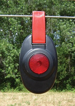 Patriot Red and black fence light-like device hanging on a wire with green trees in the background