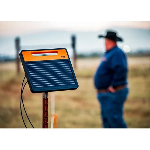 Gallagher S120 Solar fence charger on a post with a fat cattle rancher in a cowboy hat in the background