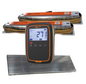 A W-O Gallagher livestock and cattle scale indicator with a black and orange casing, displaying a cattle weigh scale reading of 27i pounds , shown in front of an alleyway loadbar set on a white background. and cattle weigh platform