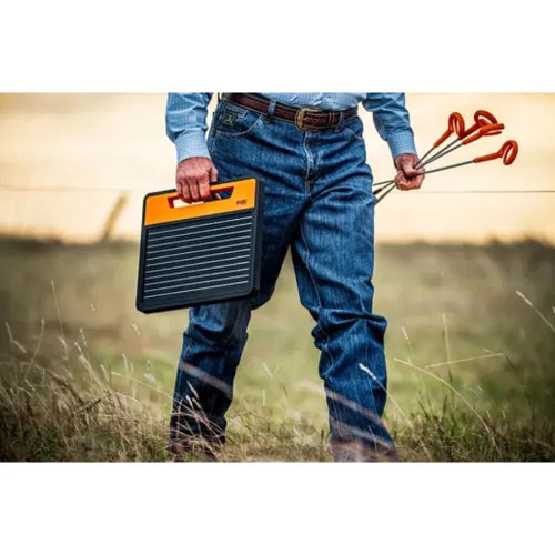 farmer holding a Gallagher S120 solar panel fence charger and posts in a field